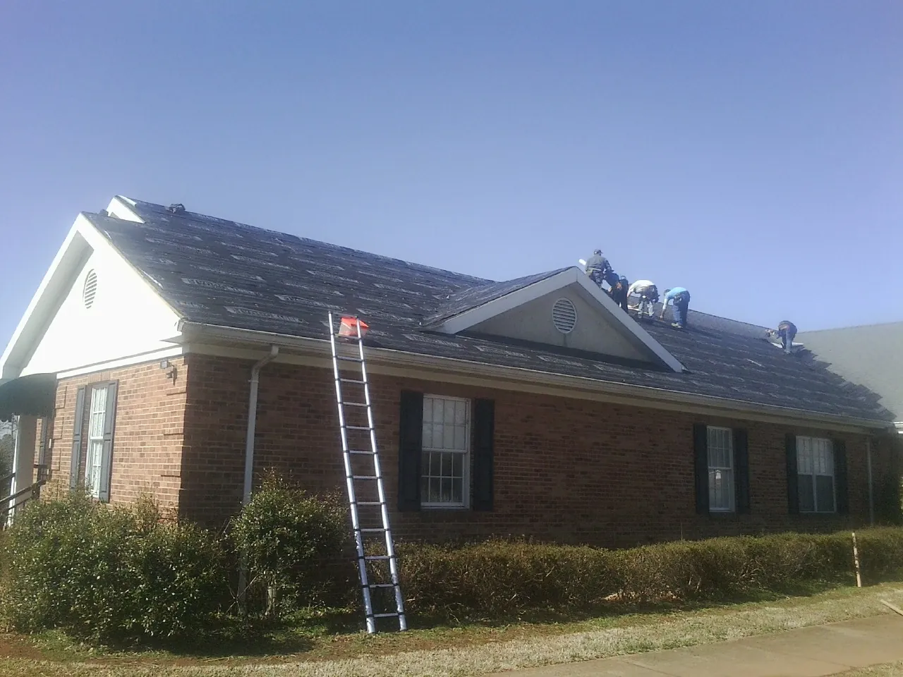 Crew tearing shingles off a brick ranch roof with a ladder set — Metal Roof Repair work by our crew in New Vernon