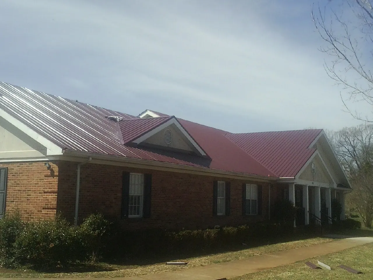 Red metal roof with gabled entries on a long brick building, from a Hail Damage Roof Repair job in New Vernon