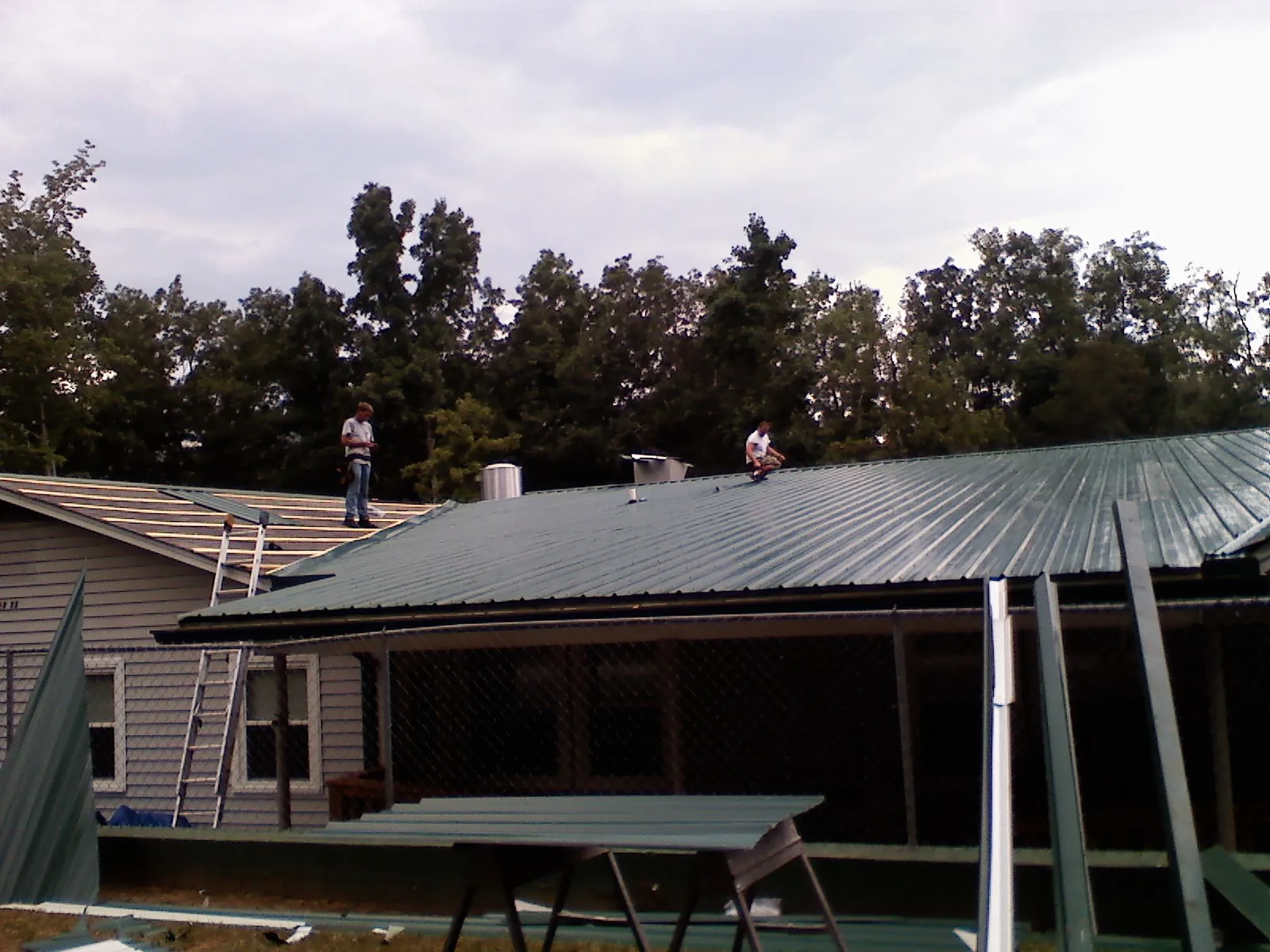 Two roofers installing green metal panels above a covered porch in New Vernon