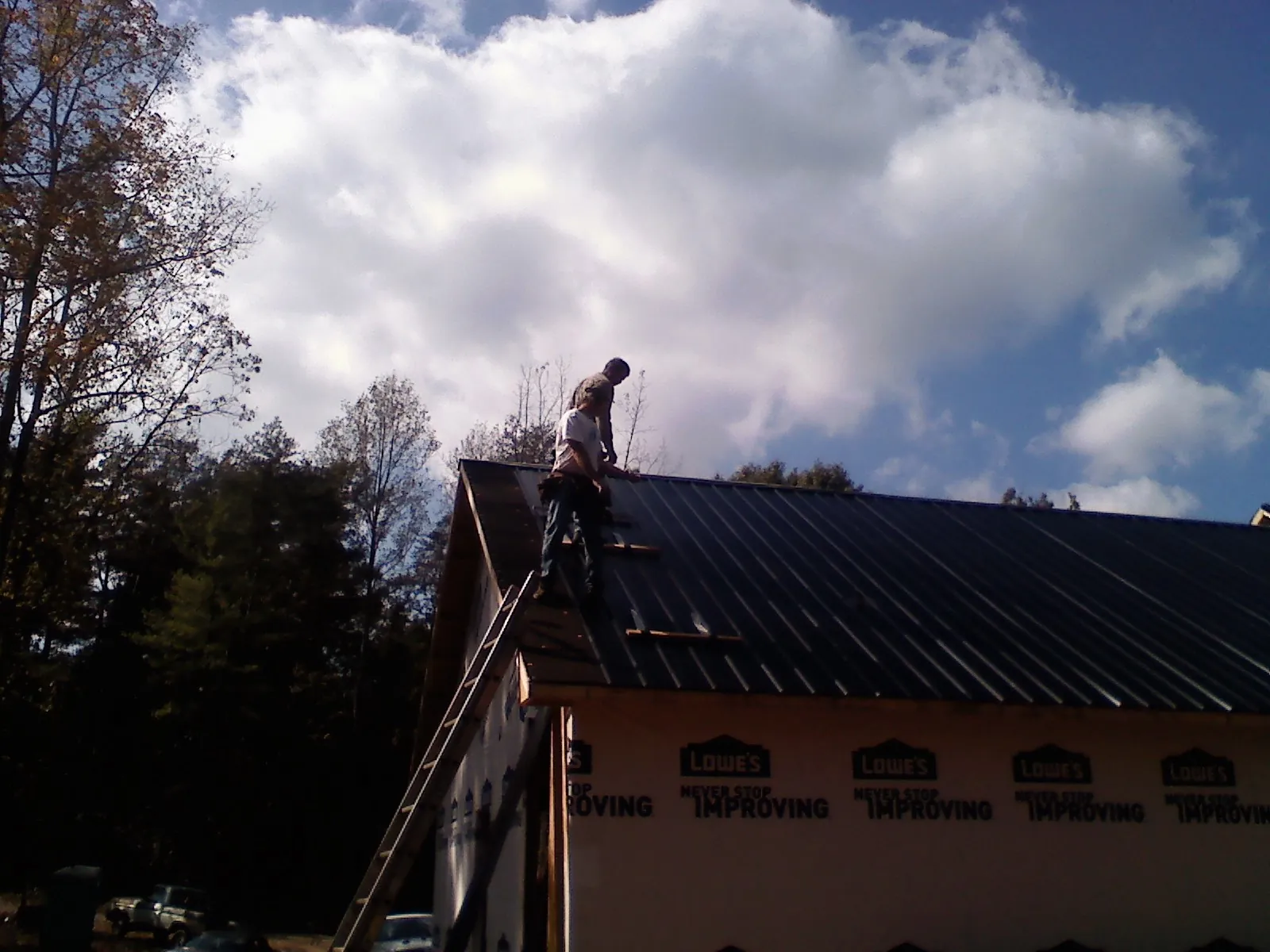 Roofer fastening dark metal panels high against a cloudy sky, from a Roof Inspection job in New Vernon