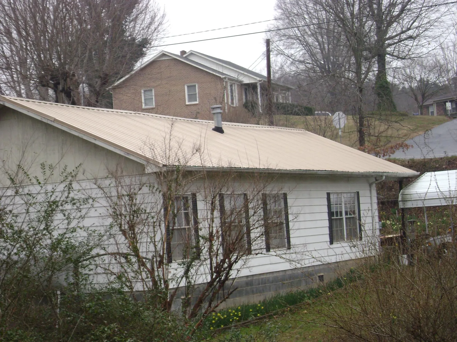 Tan metal roof on a white sided house set into a hillside — Commercial Roofing by Roofing Brothers in New Vernon